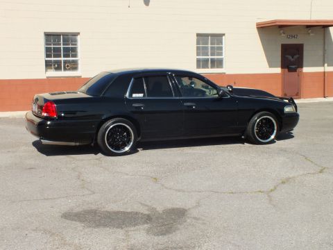 2003 Ford Crown Victoria - Rear three-quarter of a black Crown Victoria sedan on black wheels beside a beige unit numbered 12942.