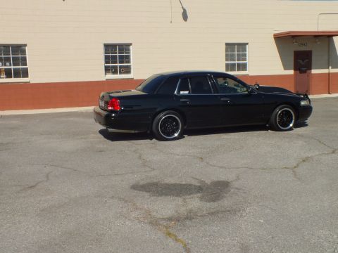 2003 Ford Crown Victoria - Black Crown Victoria sedan parked at an angle on a cracked parking lot in front of a beige building.