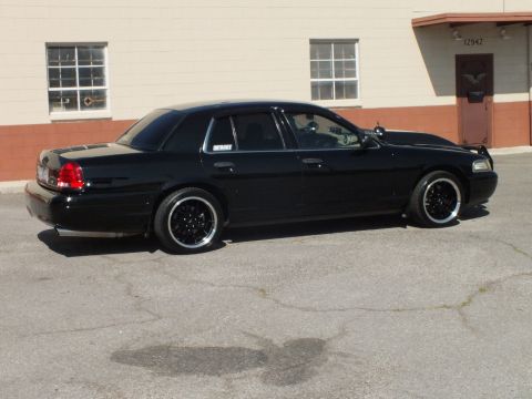 2003 Ford Crown Victoria - Passenger-rear view of a lowered black Crown Victoria with red taillights against a beige wall.
