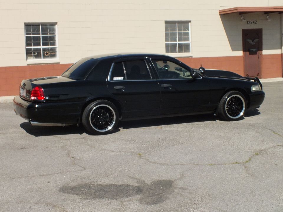 Black Crown Victoria passenger-rear three-quarter, lowered on black wheels, beige building 12942