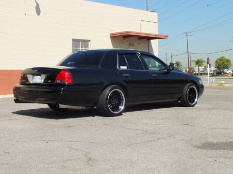 2003 Ford Crown Victoria - Rear three-quarter of a black Crown Victoria showing Ford oval and SVT badge on black wheels.