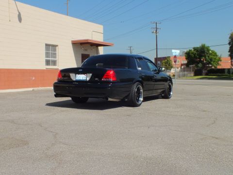 2003 Ford Crown Victoria - Rear three-quarter of a black Crown Victoria sedan with SVT badge parked on an empty asphalt lot.