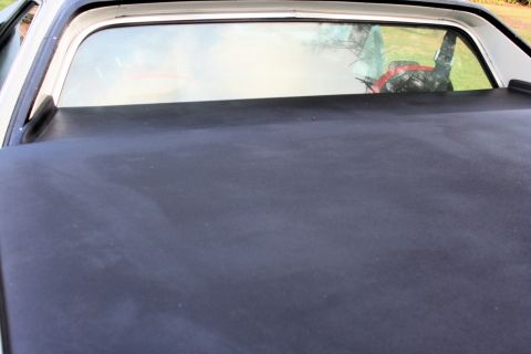 1976 Ford Ranchero - The bedcover of a 1976 Ford Ranchero is visible, along with the rear window reflecting the outdoors.