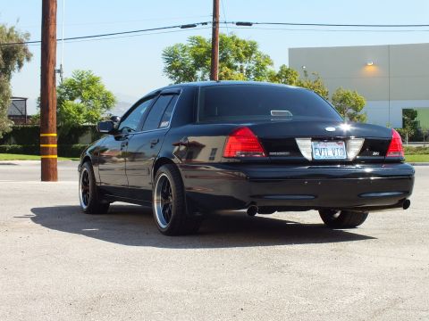 2003 Ford Crown Victoria - Driver-rear three-quarter of a black Crown Victoria with SVT badge in front of a light industrial building.