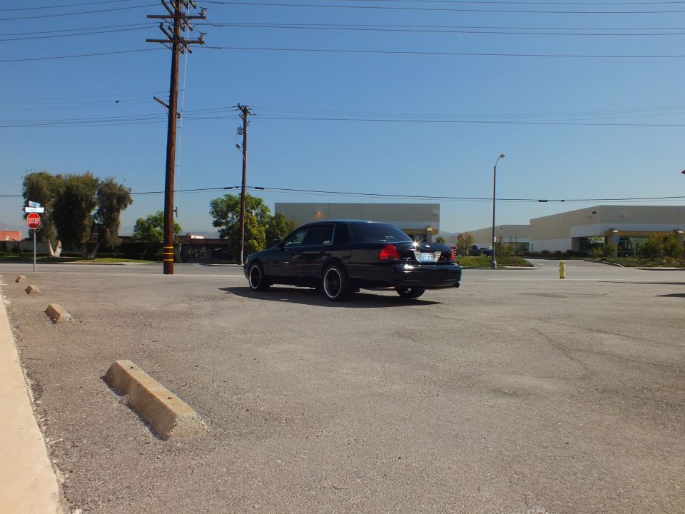Black Ford Crown Victoria sedan parked at distance in empty industrial lot under blue sky