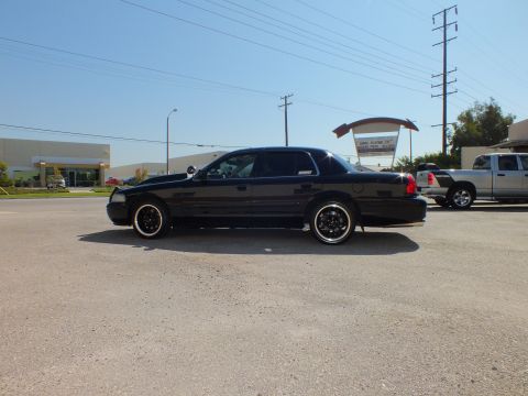2003 Ford Crown Victoria - Lowered black sedan shown in profile on black multi-spoke wheels with whitewall tires.