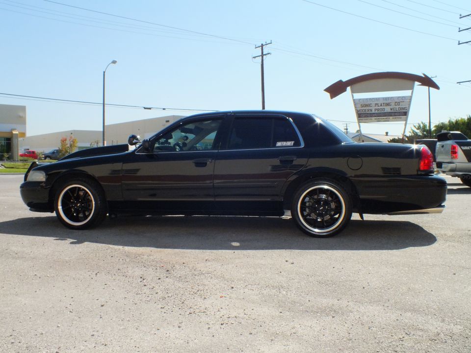 Black Crown Victoria driver-side profile on black wheels at industrial yard