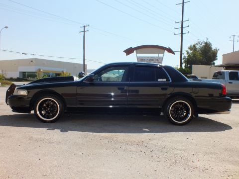 2003 Ford Crown Victoria - Lowered black sedan in profile with front grille guard and black multi-spoke wheels.