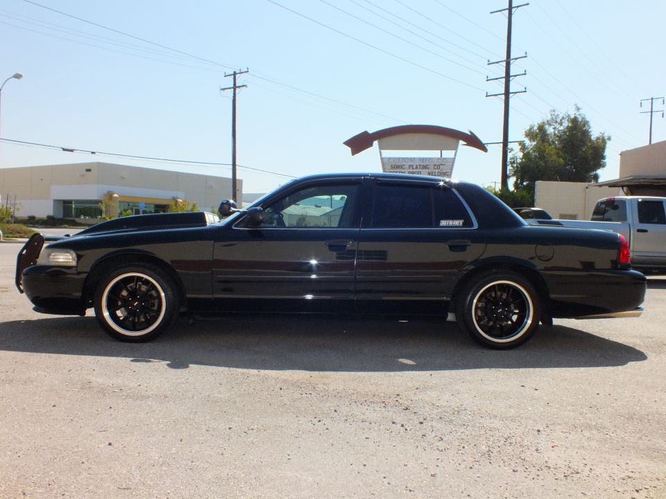 Black Crown Victoria driver-side profile with front push bar at industrial parking lot