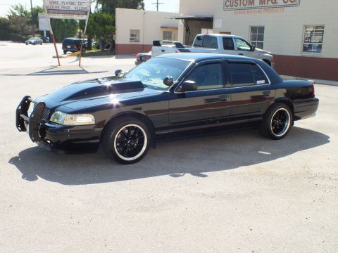 2003 Ford Crown Victoria - Front quarter of a black sedan wearing a chrome push bar, black wheels and whitewall tires.