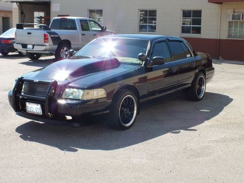 2003 Ford Crown Victoria - Sun glints off the hood of a black sedan with grille guard; California plate reads 6VTL170.