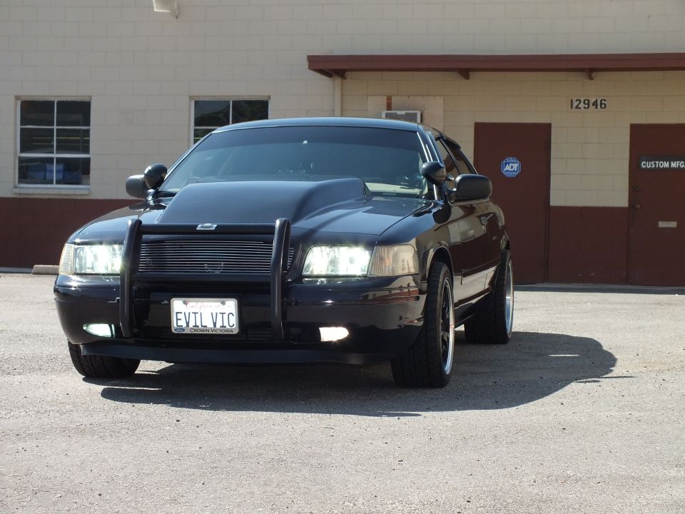Black Ford Crown Victoria front view with push bar and EVIL VIC plate by Custom Mfg building