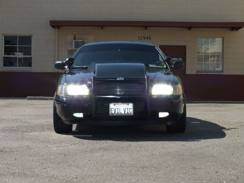 2003 Ford Crown Victoria - Black sedan photographed head-on with headlights lit, billet grille and EVIL VIC vanity plate.