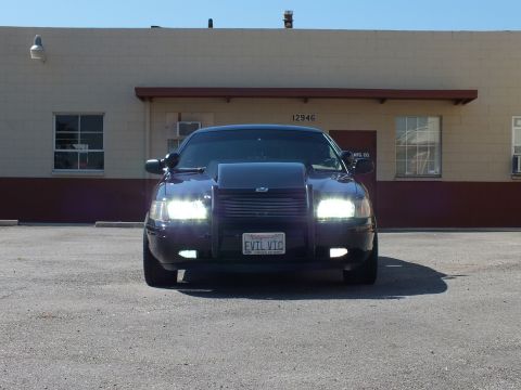2003 Ford Crown Victoria - Black sedan shown head-on with headlights on and an EVIL VIC California vanity plate.