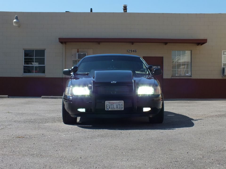 Black Crown Victoria head-on with headlights illuminated and EVIL VIC California plate
