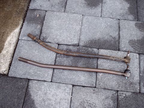 1996 Ford Bronco - Two tie rods, one significantly more corroded than the other, are laid out on a grey paver stone surface.