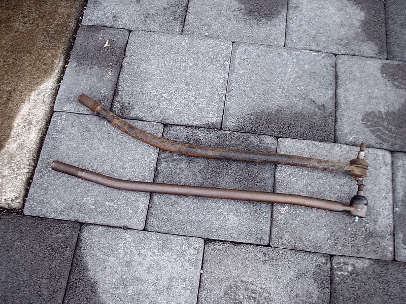 Two rusty steering tie rods/drag link on gray pavers
