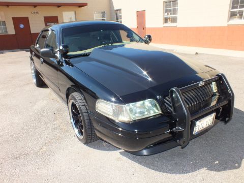 2003 Ford Crown Victoria - Front three-quarter of a black full-size Ford sedan fitted with a chrome push bumper and dark aftermarket wheels.