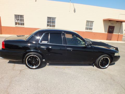 2003 Ford Crown Victoria - Passenger-side profile of the black sedan with window rain visors and gloss-black aftermarket wheels.