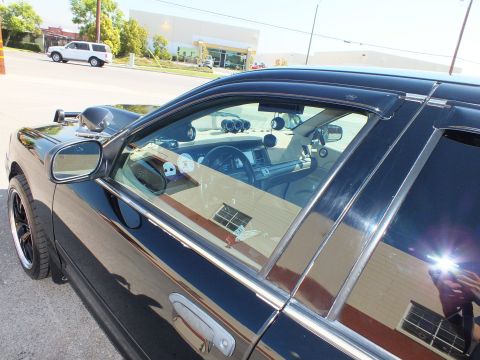 2003 Ford Crown Victoria - Side glass of the black sedan with rain visors, showing the tan interior and added gauges within.