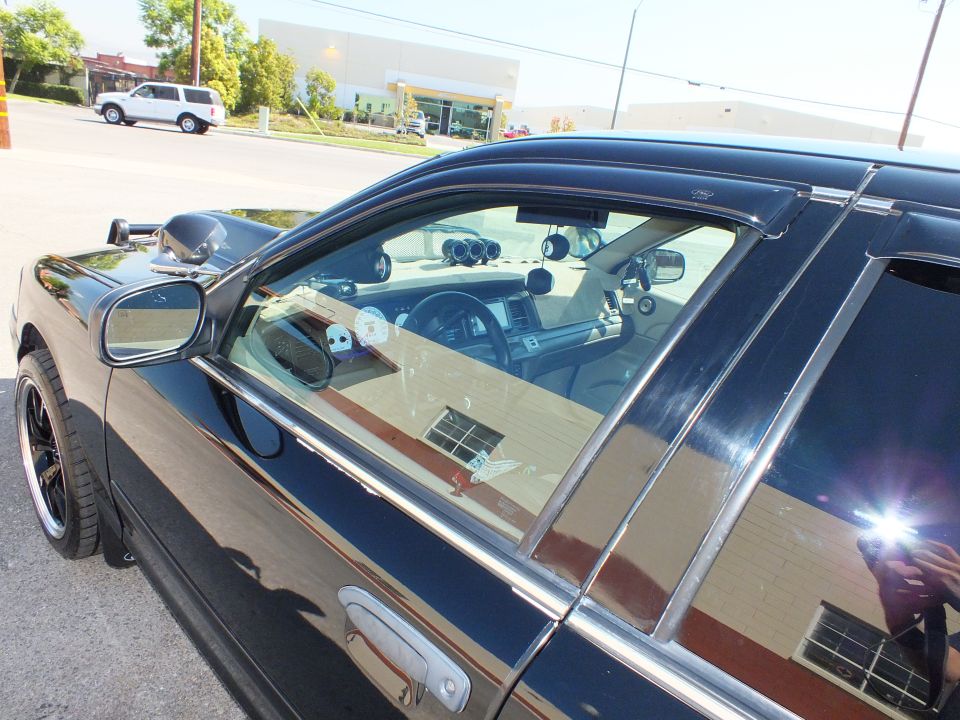 Black sedan door and window glass with rain visors revealing tan interior and gauges