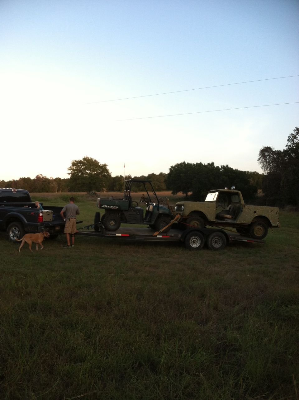 Tan pickup truck towing trailer with utility vehicle and vintage SUV