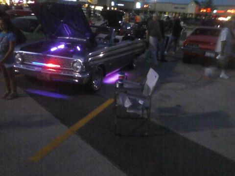 2003 Ford Crown Victoria - A classic car is displayed with its hood up and illuminated by purple and red lights, parked outdoors at an event.