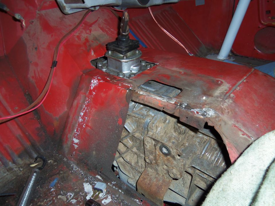 Vehicle interior showing a manual transmission shifter and red painted floor panels with rust and modifications