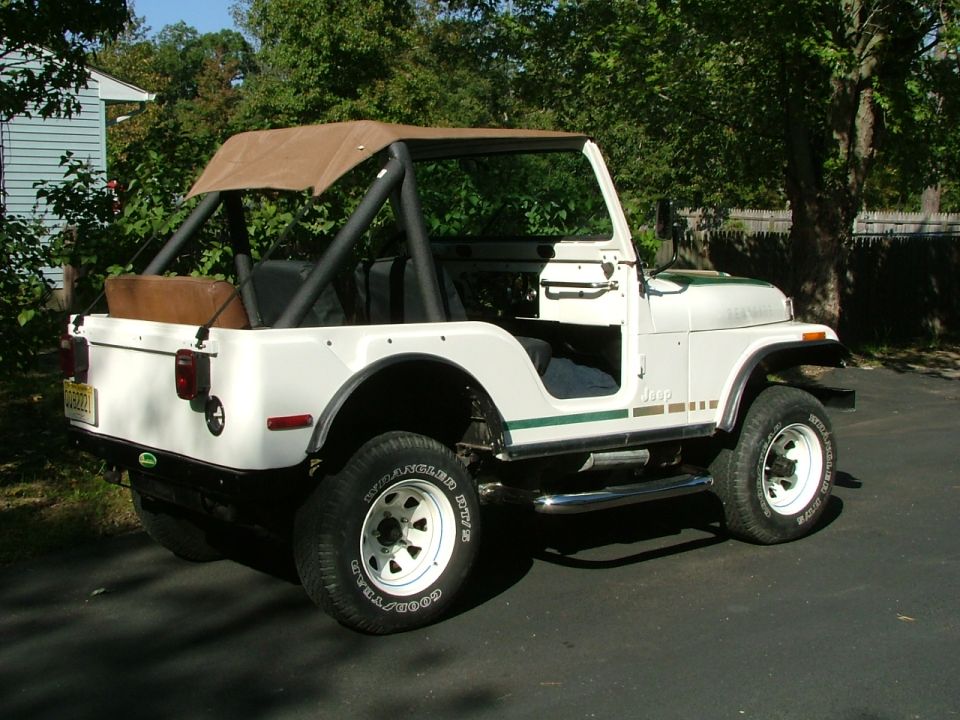 White Jeep CJ5 with brown soft top and green stripe, parked on asphalt driveway