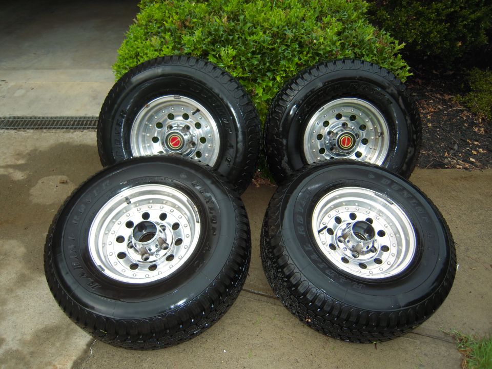 Four polished slotted alloy wheels with Dunlop Radial Rover tires on a driveway