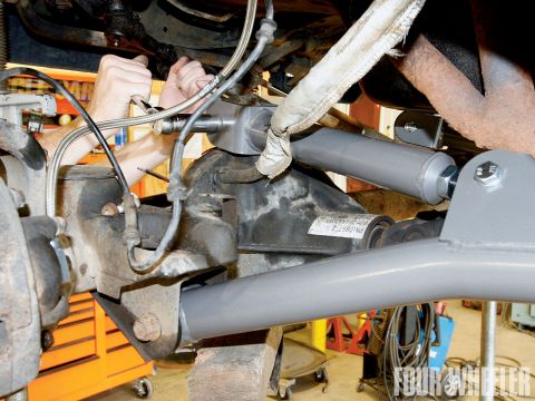 1968 Ford Bronco - Mechanic's hands work on the suspension system of a vehicle, focusing on the rear axle and shock absorbers.