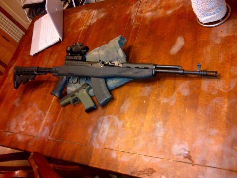 1989 Ford Bronco - An SKS rifle and a handgun are laid out on a wooden table, with a laptop in the background.