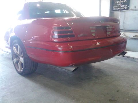 1999 Ford Crown Victoria - The rear of a red sedan is shown, custom taillights and a spoiler, parked inside a garage.