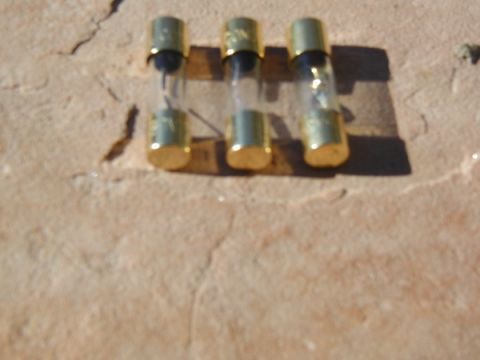 1998 Ford Taurus - Three glass fuses with brass caps are laid out on a textured surface, possibly for a vehicle's audio system.