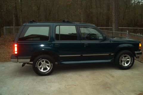 1992 Ford Bronco - This SUV is seen from the side, parked on a concrete driveway with trees in the background.