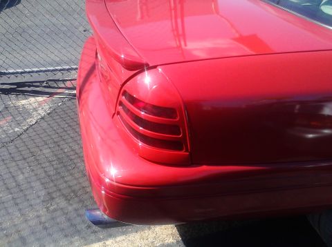 1999 Ford Crown Victoria - Close-up of a red sedan's rear, showing the taillight and exhaust pipe.