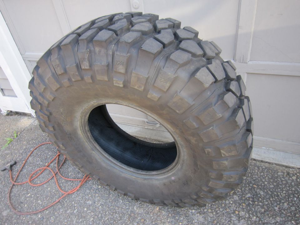 Large off-road tire with aggressive tread pattern, lying on concrete next to an orange cord
