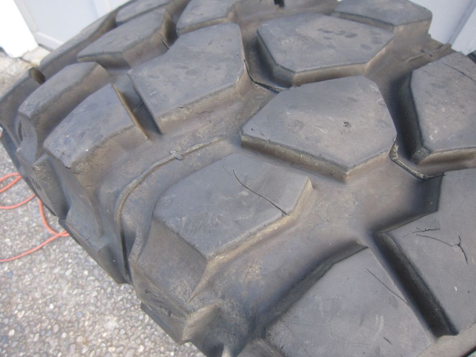 Close-up of a large, worn off-road tire tread with deep, hexagonal lugs and visible cracking