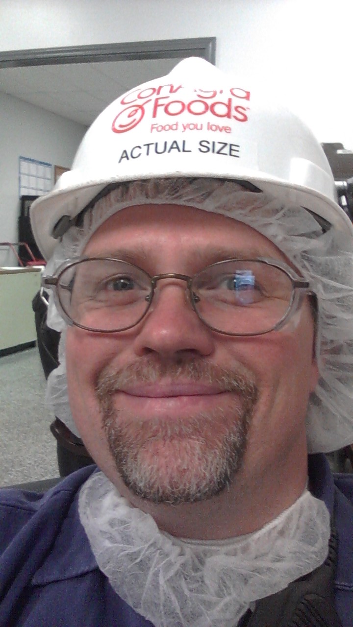 Man in blue shirt, hard hat with Con-Agra Foods logo, and hair net smiles