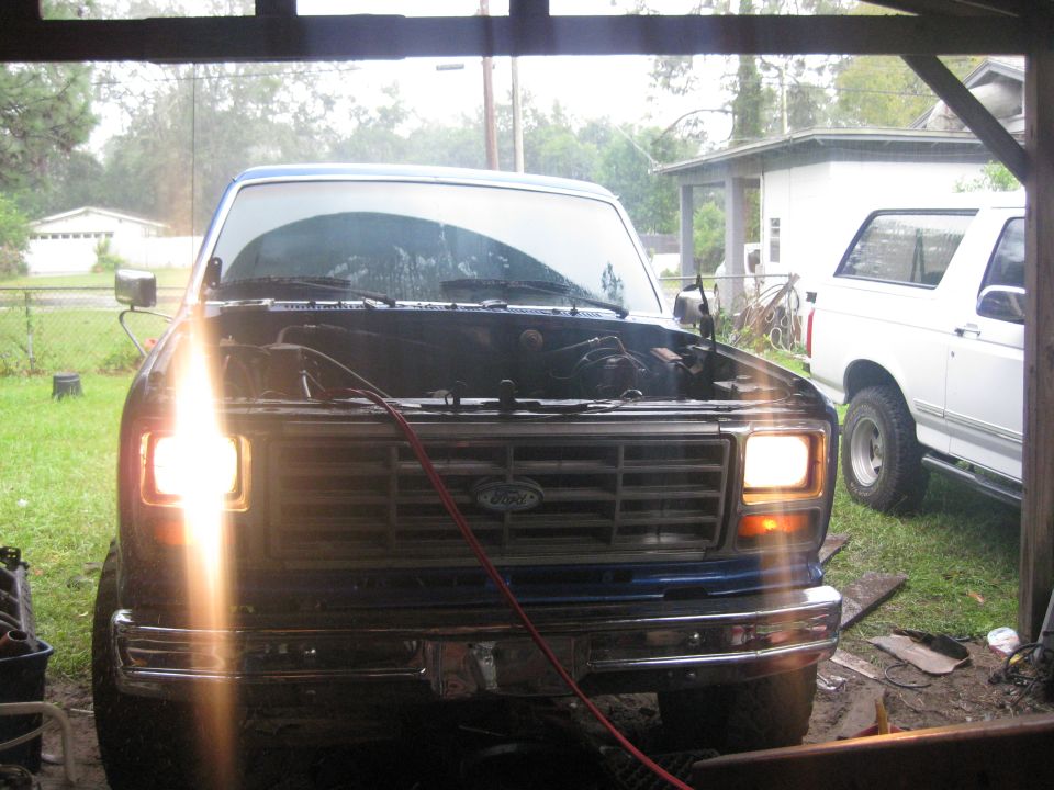 Blue Ford Bronco with hood open, parked next to a white Bronco in a garage
