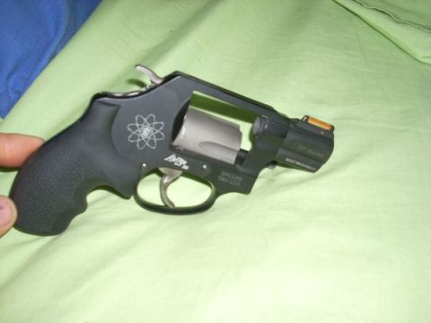 1987 Ford F-250 - A black revolver with an atomic symbol engraved on the side is held against a green fabric background.