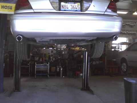 2003 Ford Crown Victoria - The rear of a silver sedan is raised on a car lift in a garage, revealing its undercarriage and exhaust system.
