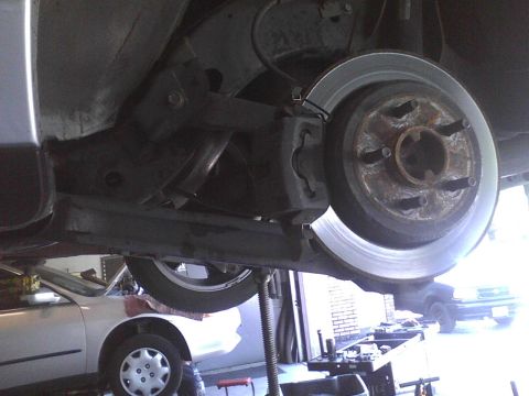 2003 Ford Crown Victoria - Close-up of a vehicle's rear brake rotor and caliper assembly, with another car in the background.