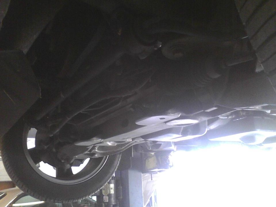 Undercarriage of a vehicle on a lift, showing suspension and exhaust components, with a tire visible