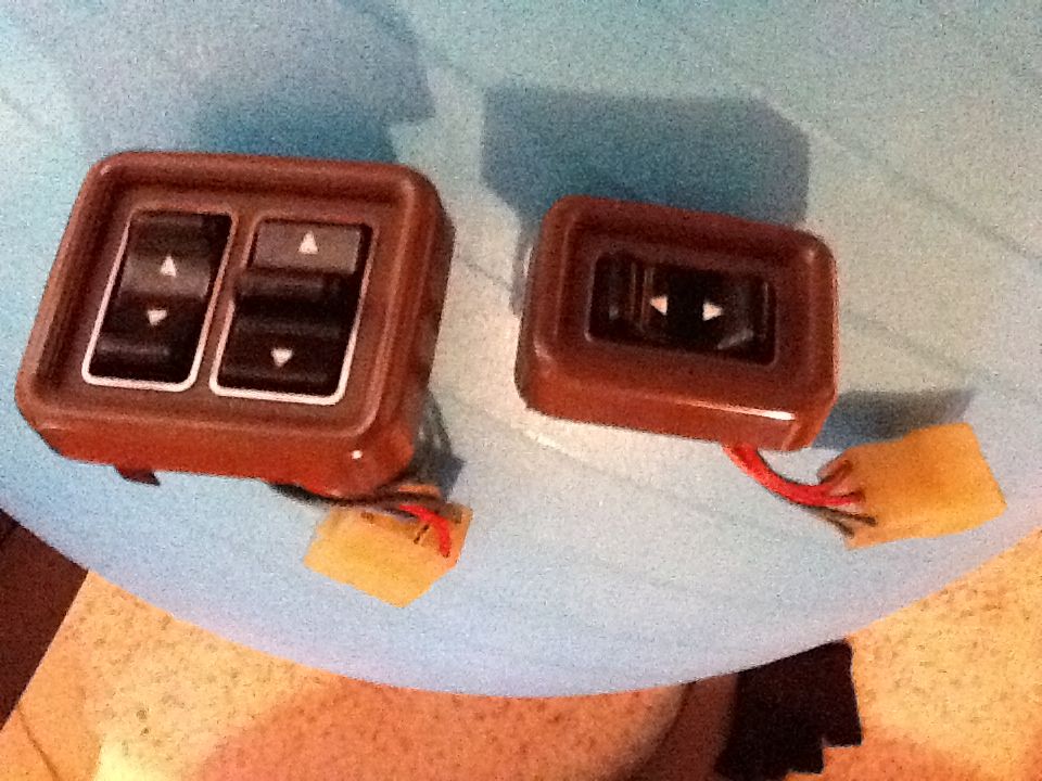 Two brown plastic power window switch assemblies with up and down arrows, one with two switches, the other with one