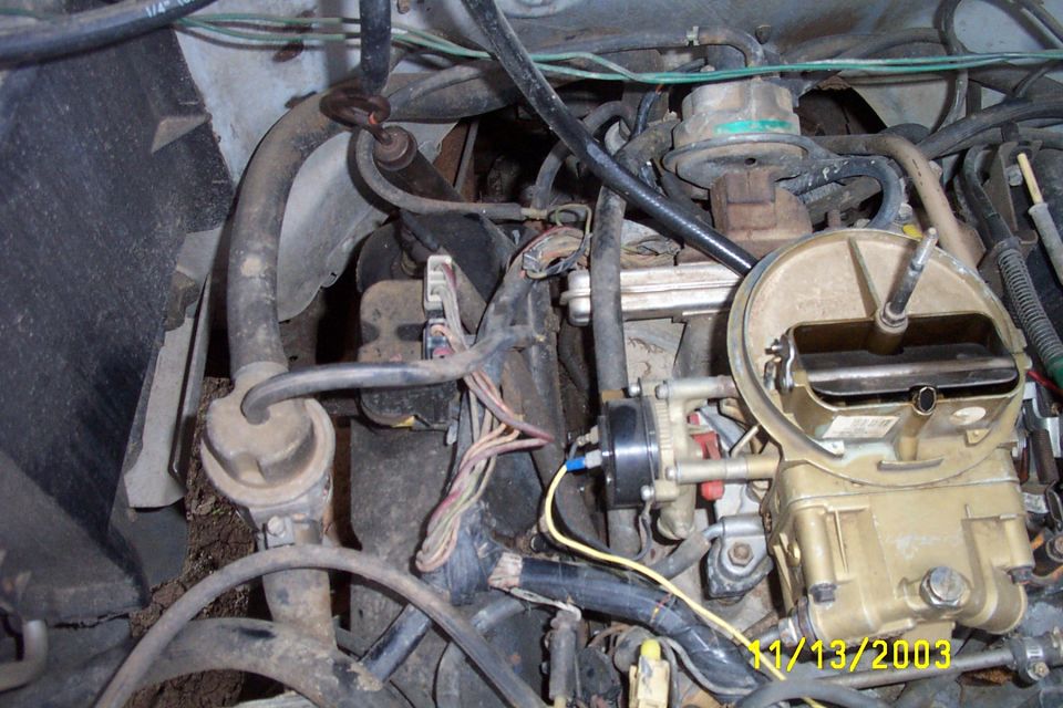 Close-up of a vehicle's engine bay, focusing on the carburetor and various hoses and wires