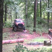 1978 Ford Bronco - A red off-road SUV is parked in a forest clearing surrounded by trees and logs.