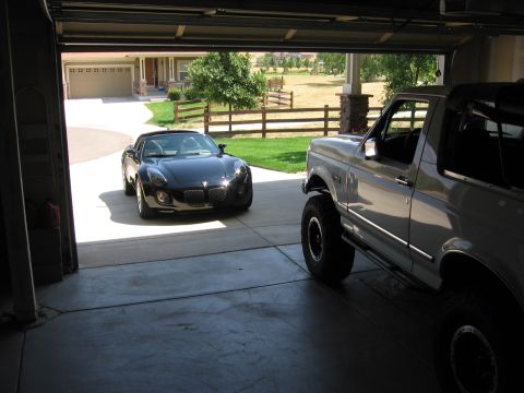 1995 Ford Bronco - Two vehicles, a Ford Bronco and a Pontiac Solstice, are parked in an open garage.
