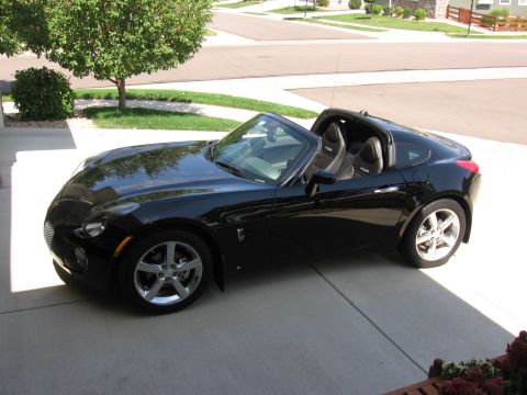 1995 Ford Bronco - A black convertible sports car is parked in a driveway on a sunny day.