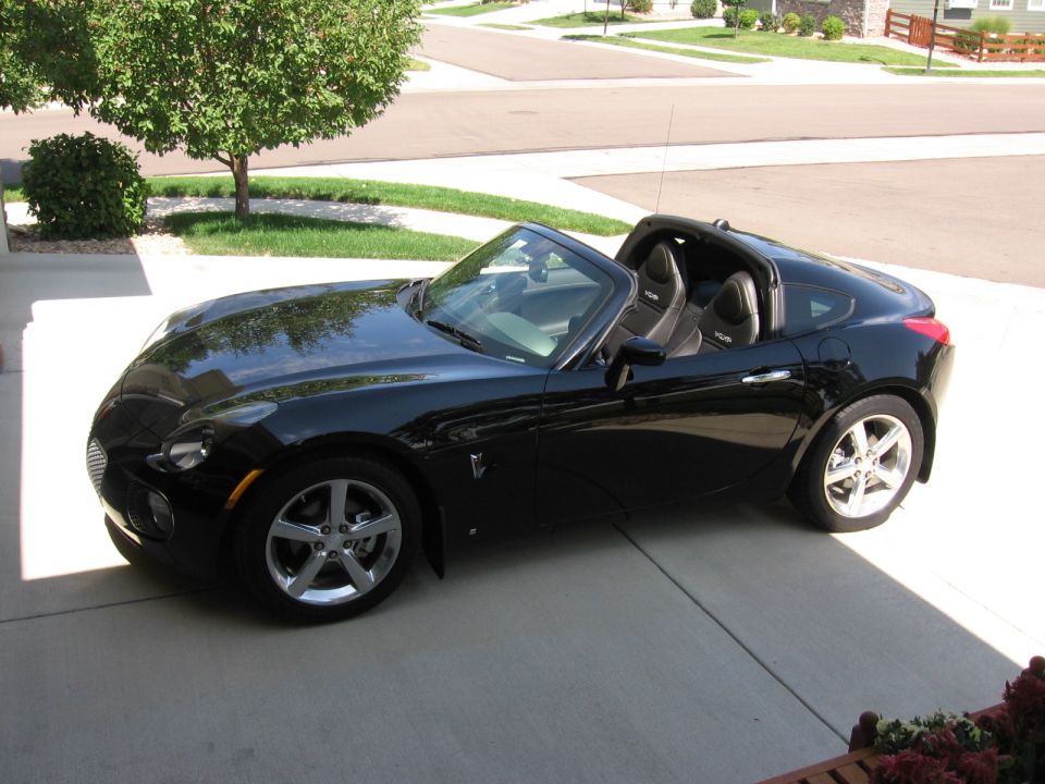 Black Pontiac Solstice coupe on a driveway, roof panel off, seen from above